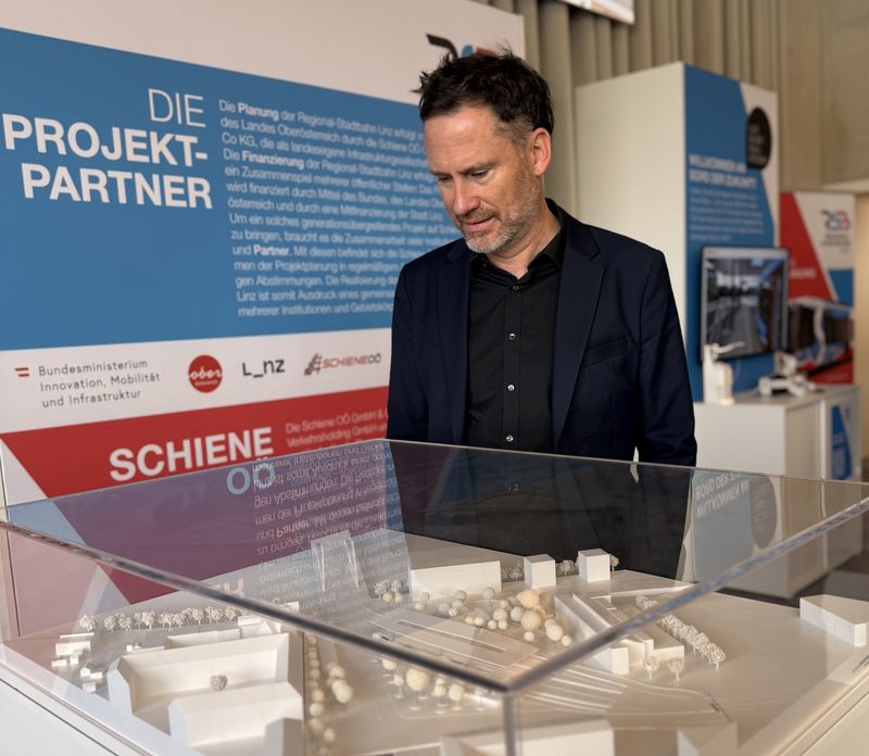 Helge Langer betrachtet in einer Ausstellung zur Regional-Stadtbahn ein weißes Architekturmodell unter einer Glashaube