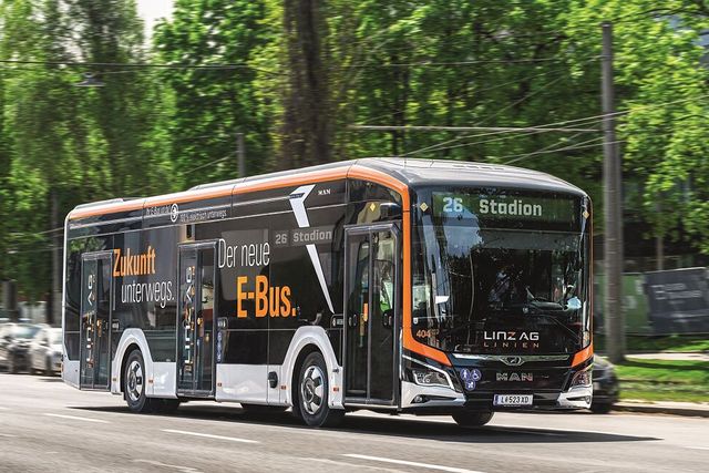 Ein neuer vollelektrischer Autobus der LINZ AG LINIEN mit der Aufschrift „Zukunft unterwegs. Der neue E-Bus.“ und der Zielanzeige „26 Stadion“ fährt eine von Bäumen gesäumte Straße entlang