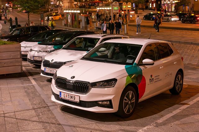 Mehrere weiße Carsharing-Autos mit dem tim-Logo und Kennzeichen „L-TIM“ stehen am Abend auf reservierten Stellplätzen am Linzer Hauptplatz