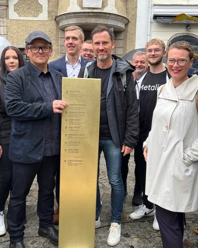 Helge Langer und weitere Gäste stehen bei der Einweihung um eine Erinnerungsstele aus Messing vor einem Altstadthaus