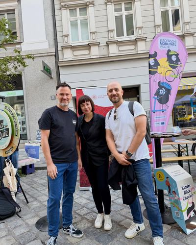 Helge Langer steht mit zwei Gästen des Mobilitätsfests vor Infoständen und Fahnen auf dem Pflaster der Domgasse