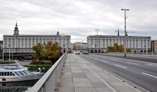 Blick über die Nibelungenbrücke auf die beiden Brückenkopfgebäude am Linzer Hauptplatz, zwei lange, gleich gebaute Gebäude zu beiden Seiten der Fahrbahn