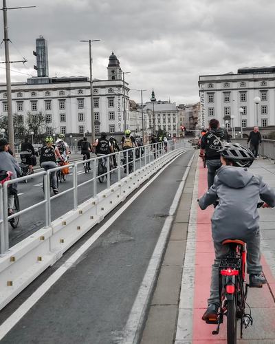 Radfahrende, vorne ein Kind mit Helm, fahren auf dem rot markierten, mit Leitwänden abgetrennten Radstreifen über die Nibelungenbrücke, im Hintergrund die Brückenkopfgebäude