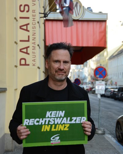 Helge Langer hält vor dem Palais Kaufmännischer Verein ein grünes Schild mit der Aufschrift „Kein Rechtswalzer in Linz“